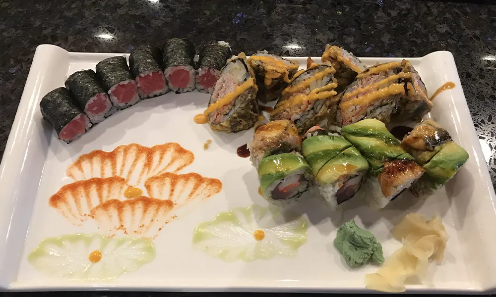 Assorted sushi platter with tuna maki, avocado rolls, tempura rolls and decorative sauce art on rectangular white plate at Sakura Japanese Restaurant, a Japanese restaurant in Wilmington