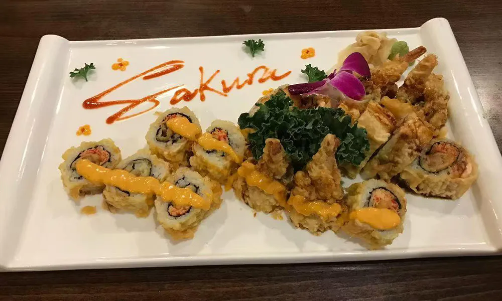 Signature tempura crab sushi roll platter garnished with purple orchid, kale and branded Sakura sauce lettering on white plate at Sakura Japanese Restaurant, a Japanese restaurant in Wilmington